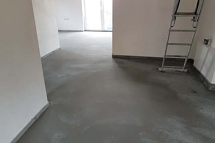 Innenraumaufnahme: Blick in einen unfertigen Wohnraum mit frisch gegossenem, glattem dunklem Estrichboden.  