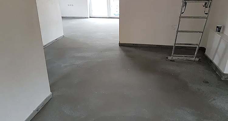 Foto: Innenraumaufnahme: Blick in einen unfertigen Wohnraum mit frisch gegossenem, glattem dunklem Estrichboden.  