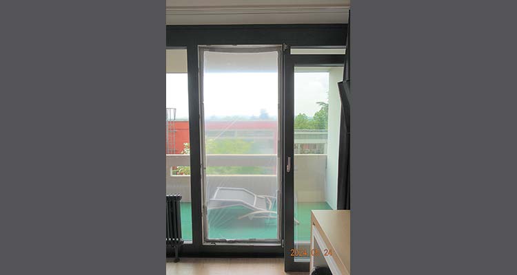 Glas-Terrassentür mit Folie abgedeckt, dahinter Balkon mit Liegestuhl und Brüstung 