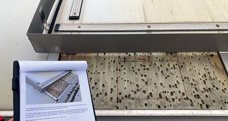 Kunststoffplatte mit vielen unregelmäßigen Löchern,  darüber eine rechtwinklige Vorrichtung zur Dokumentation der Lage der Löcher, daneben ein Klemmbrett mit Foto und Text als Anleitung oder Beschreibung 