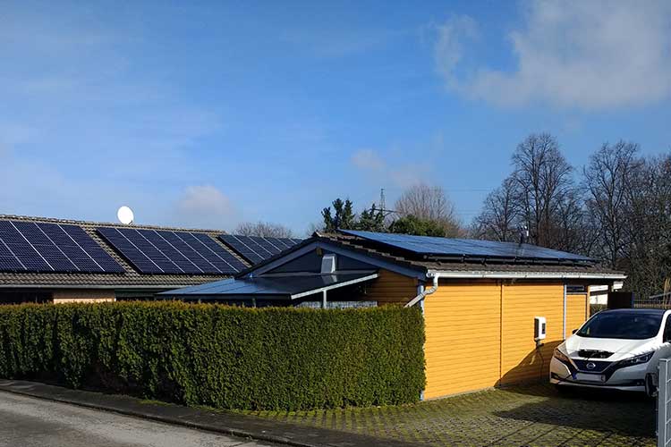 Das Bild zeigt ein Haus und eine Garage mit Pfotovoltaikanlage auf dem Dach und ein E-Auto neben der Garage, das Strom tankt. 