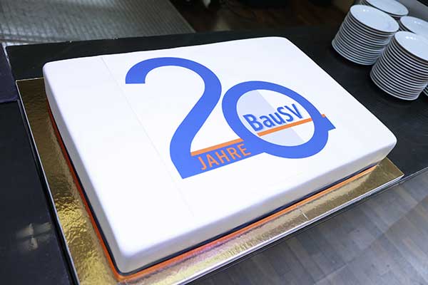 Das Bild zeigt die große rechteckige flache weiße Geburtstagstorte mit der Aufschrift 20 Jahre BauSV in Blau.