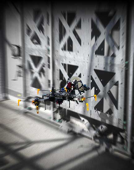 Das Bild zeigt eine Drohne an der Testwand im DroneHub mit modularen Bauelementen für Versuche mit fliegenden Baurobotern. 