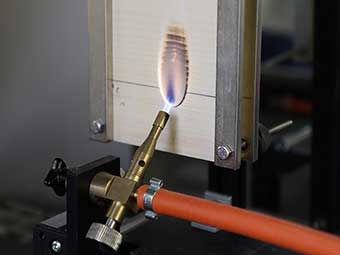 Das Bild zeigt den Einzelflammentest nach EN-ISO 11925-2 für die flammschützende Wirkung der neuen Holzbeschichtung im Brandlabor des Fraunhofer WKI am Beispiel von Fichtensperrholz. 