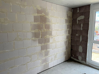 Foto: Wand aus weißlich-beigen Porenbetonsteinen in einem Rohbau. In der Mitte ist eine große dunklere Stelle, die von einem Feuchteschaden herrührt. 