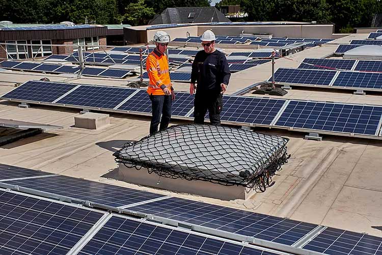 Zwei Personen mit Helmen stehen auf einem Flachdach mit installierten Solarpaneelen.  