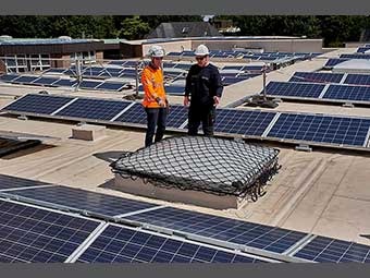 Zwei Personen mit Helmen stehen auf einem Flachdach mit installierten Solarpaneelen.  