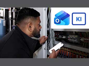 Eine Person mit einem Smartphone steht vor einem geöffneten Schaltschrank. Oben rechts sind das Outlook-Symbol und ein KI-Icon zu sehen. 