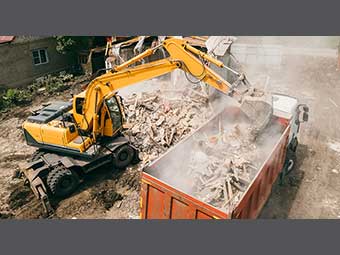 Foto: Hausabriss, ein Bagger schaufelt Bauschutt in eine Mulde. 