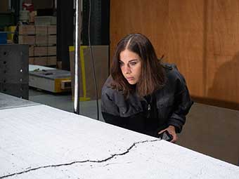 Eine Person inspiziert eine helle Betonplatte mit einer markanten Rissbildung in der Mitte. 