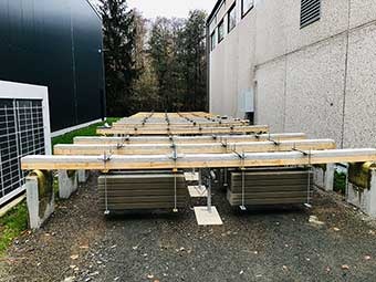 Foto: Versuch zur Untersuchung der Biegebelastung von Holzverbünden. An horizontalen Holzverbundlatten, die auf Betonfundamenten aufliegen, hängen Gewichte.  