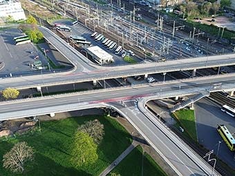 Luftbild, komplexes Verkehrsknotenpunkt-Szenario: Im Zentrum kreuzen sich aufgeständerte mehrspurige Straßenbrücken über einem dichten Bündel parallel verlaufender Eisenbahngleise. 