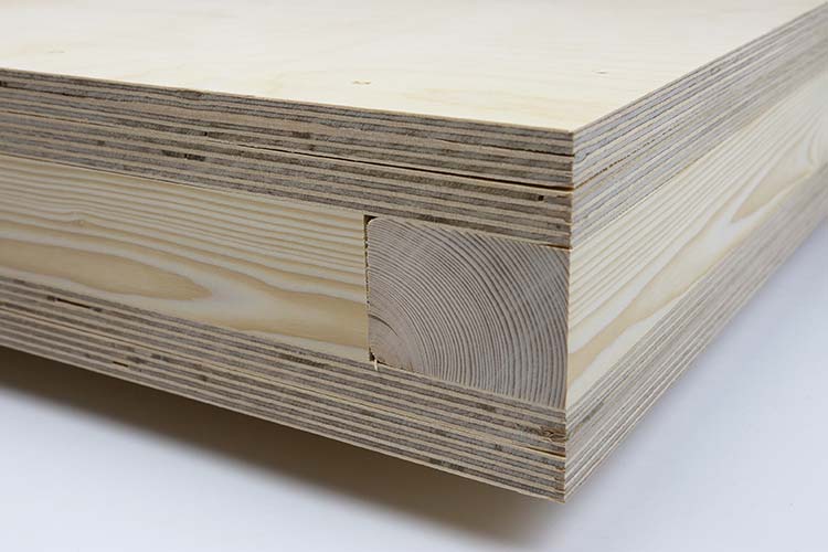 Bild, technische Detailaufnahme eines Holzbauteils: Rechteckiger Plattenquerschnitt aus mehrfach verleimten Schichten Sperrholz, horizontal geschichtet. In der vorderen Kante ist mittig ein massives Kantholz bündig eingelassen, umgeben von den Sperrholzlagen. 