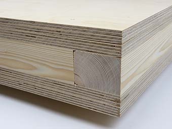 Bild, technische Detailaufnahme eines Holzbauteils: Rechteckiger Plattenquerschnitt aus mehrfach verleimten Schichten Sperrholz, horizontal geschichtet. In der vorderen Kante ist mittig ein massives Kantholz bündig eingelassen, umgeben von den Sperrholzlagen. 