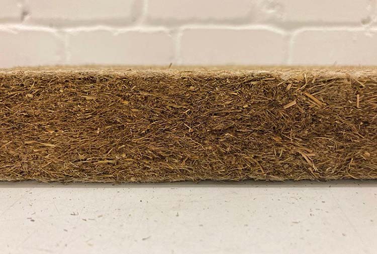 Foto: Matte aus braun-beigen gepressten Fasern vor weißer Backsteinwand 
