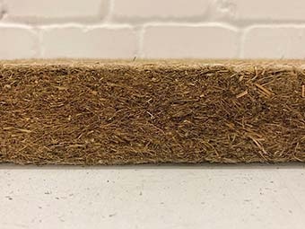 Foto: Matte aus braun-beigen gepressten Fasern vor weißer Backsteinwand 