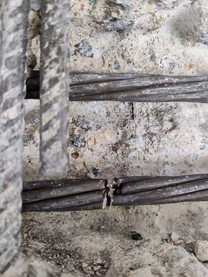 Betonoberfläche mit mehreren horizontal verlaufenden Bewehrungsstäben, von denen ein Bündel mittig sichtbar beschädigt oder unterbrochen ist 
