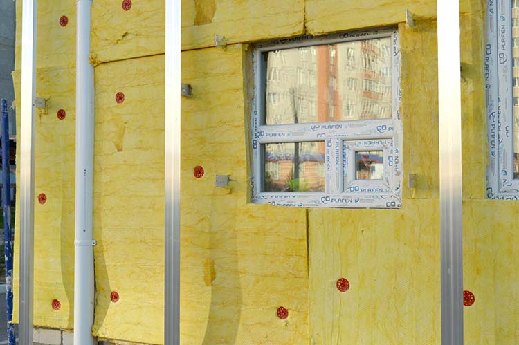Rohbauwand mit Fensterausschnitt und aufgebrachten gelben Platten zur Wärmedämmung, davor Aluprofile 