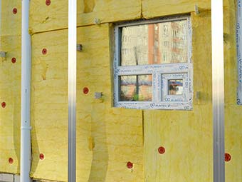 Rohbauwand mit Fensterausschnitt und aufgebrachten gelben Platten zur Wärmedämmung, davor Aluprofile 