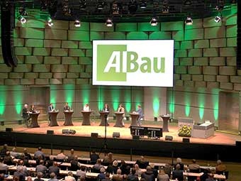 Großer Veranstaltungssaal mit 7 Pulten, an denen Redner stehen. Blick aus den Publikumsreihen zur Bühne. 